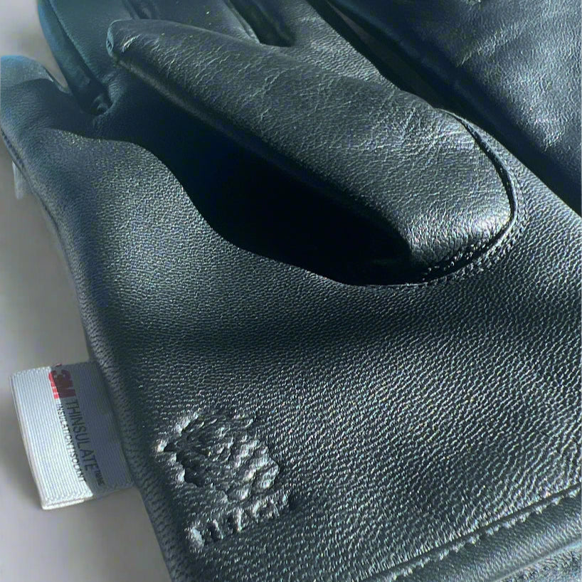 Black leather gloves with a brand logo on a textured surface