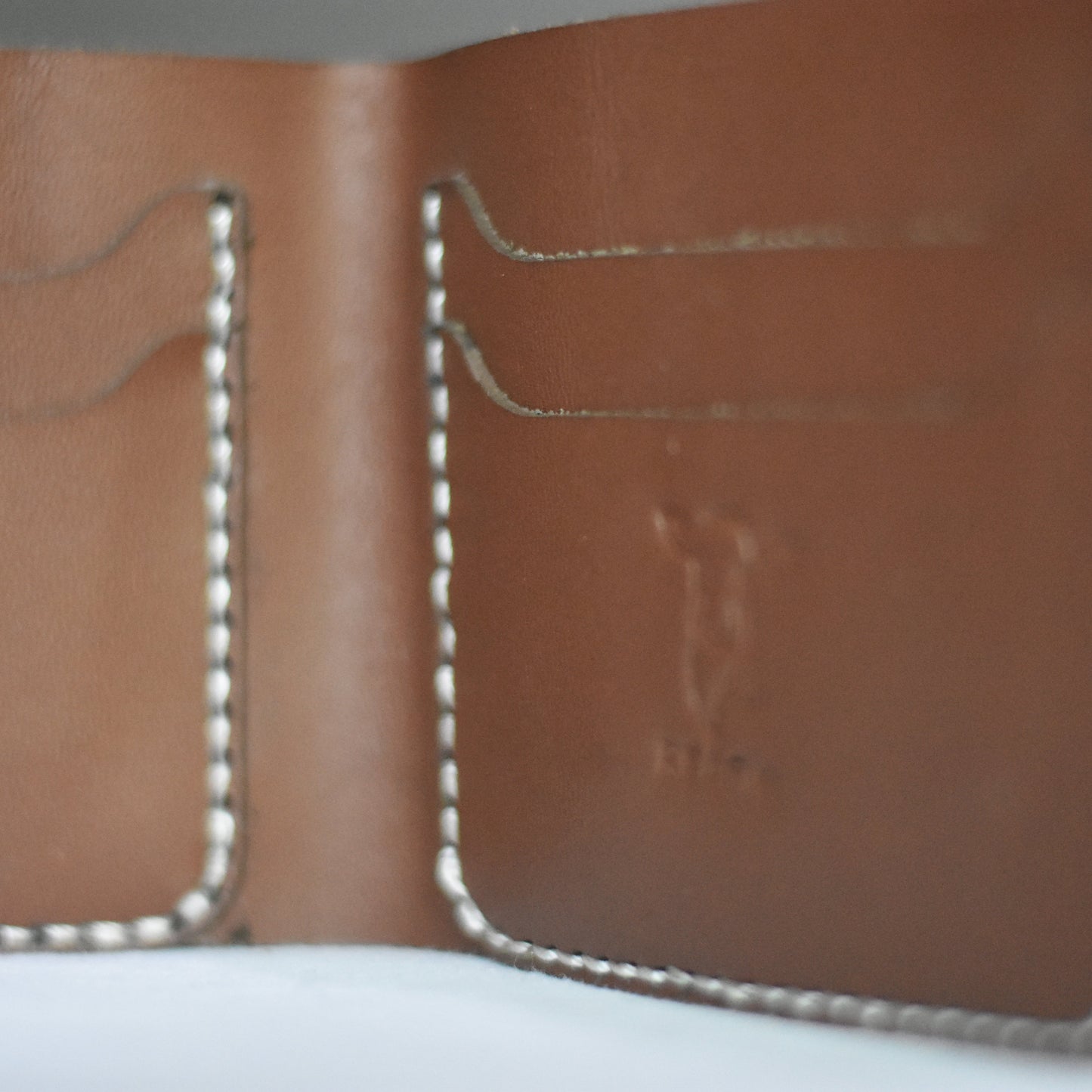 Close-up of a brown leather wallet with stitching details on a white surface.