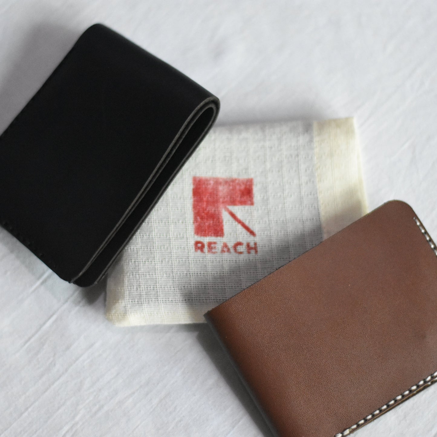 Black and brown wallets on a textured surface with 'REACH' branding.