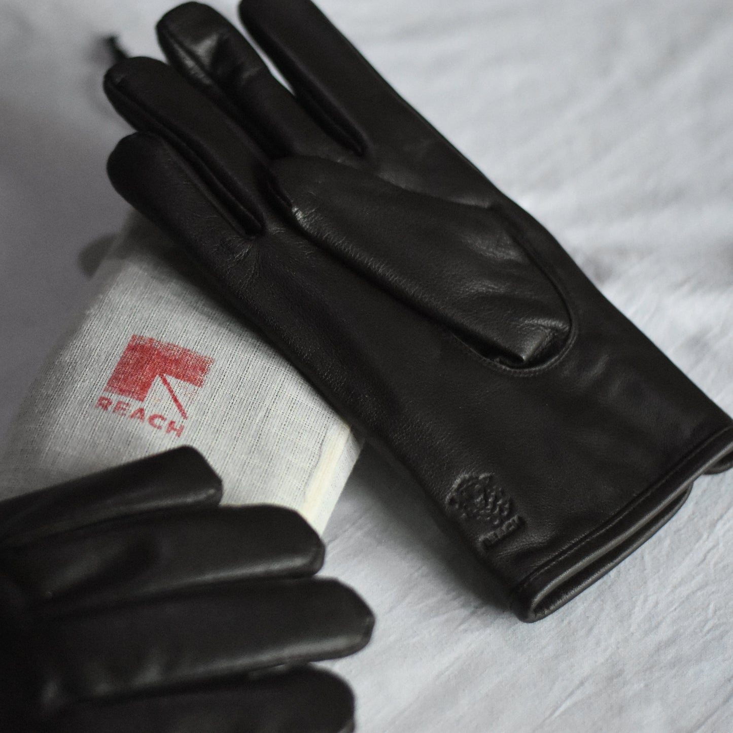 Black leather gloves on a white surface with a visible brand logo.