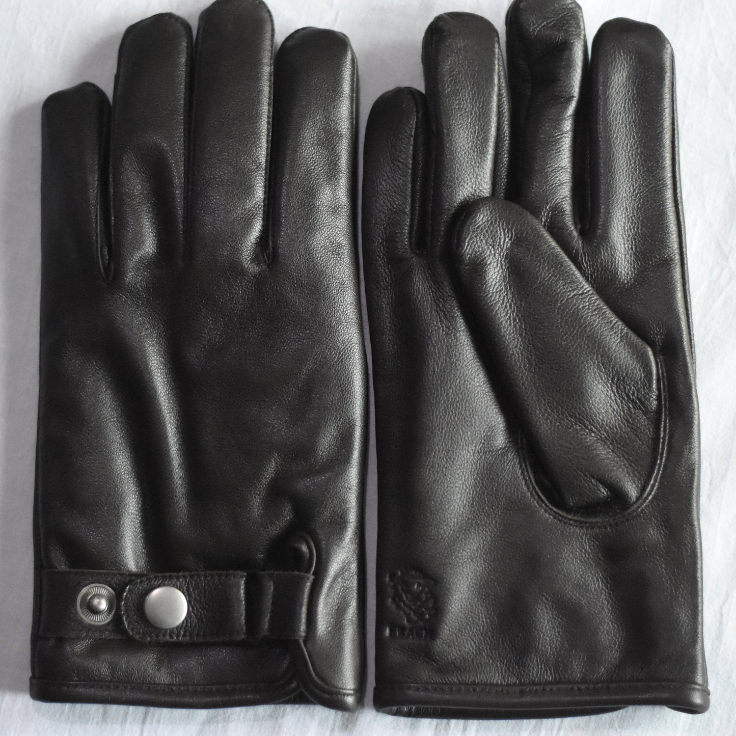 Pair of black leather gloves on a light wooden surface