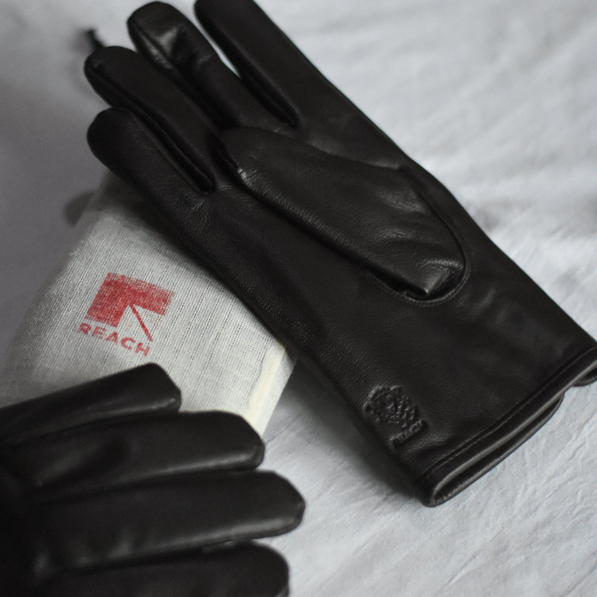 Black leather gloves on a white surface with a visible brand logo.